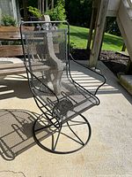 Full side angle view of the black metal rocking chair showing the mesh seat, backrest, armrests, and circular rocking base