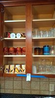 Photo of cabinet shelves with various drinking glasses and ceramic mugs showing multiple colors and styles.