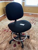 Front view of black swivel office chair showing fabric seat, backrest, and circular metal footrest ring.