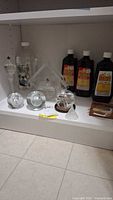 Clear glass oil lamps and three bottles of lamp oil arranged on shelf.