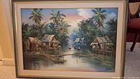 Framed original painting showing water, boats, huts, palm trees, and surrounding foliage.