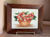 Overall photo of framed theorem painting depicting strawberries in a basket with metal stand.
