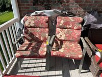 Two patio chairs with floral cushions and metal frames, placed on a covered deck with visible weathering and fading on cushions.