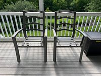 Two gray metal ladder-back patio chairs with curved armrests stacked together on deck flooring.