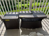 Photo taken outdoors showing the all weather wicker patio table and the plastic storage box side by side on a wooden deck, highlighting their size and condition.