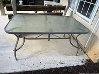 Front side view of rectangular patio table with glass top, showing metal frame and curved legs.