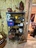 Wide view of metal shelving unit with assorted gardening and decorative items including planters, tools, and plant stands arranged around it.