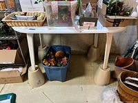 Full view of white oval plastic table in basement, showing legs and surface with marks and stains