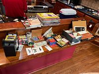 Overall view of multiple decks of cards, card games, and game accessories spread on a counter with visible card shuffler and various boxes and manuals.