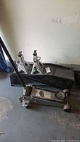 Hydraulic jack placed on floor with two jack stands and two metal ramps around it, all showing use and dirt.
