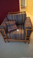 Full view of the rattan chair showing the striped cushions and plaid pillow on a carpeted floor.