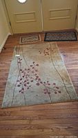 Large rug with beige background and red vine floral design laid out on wood floor
