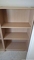 Front view of shelving unit showing three shelves and light wood finish.