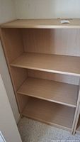 Full view of light wood tone pressed wood shelving unit with three shelves showing front and side.