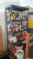 Full view of the gray plastic shelving unit holding various cleaning supplies and other containers. Shelving is sturdy with grid-pattern shelves and solid corner poles.