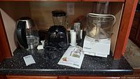 Photo showing all three appliances on a kitchen counter: electric kettle, blender, food processor with manual.