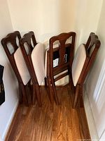 Four wooden folding dining chairs folded and stacked against a wall, showing the wood finish and upholstery.
