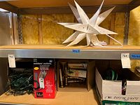 Wide shelf view showing Moravian star light, box of outdoor electrical outlets, string lights, and candle lamps.