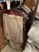 Photo of cream embroidered linen with sunflower and daisy floral design hanging on a rack with other linens in plastic covers.