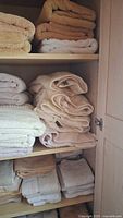 Four shelves of folded towels in neutral colors shows varying wear and some discoloration