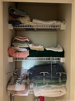 Shelving with folded towels and wash cloths of various colors including white, green, beige, pink, and patterns along with a metallic over door hook rack hanging beneath a shelf.