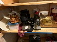 Shelving with assorted bags (brown, black), Mr Coffee plastic trays with cups, travel cake caddy, and water filter pitcher and dispenser.