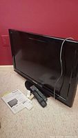 Panasonic 32-inch TV standing on carpeted floor with remote and power cord visible on side and manuals placed in front.