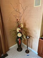 Front view of resin vase with large faux flower arrangement and metal stand beside it, showing overall height and details.