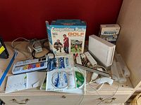 Overall lot showing Nintendo Wii console, games, remotes, sleeves, power adapter and sensor bar in a shelf.