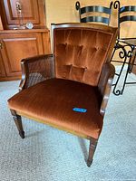 Front angle showing brown velvet tufted seat and backrest, wooden frame and caned side panels