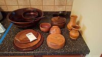 Wood bowls, vases, and containers displayed on counter. Includes large and small bowls, two vases, a lidded container, and wood spork.