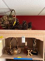 Photo showing the carved wood tea pot, golf figure, candle holder, wooden letter 'K', and a basket of faux gold and pine cones on a shelf.