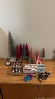 Assorted bottle brush trees, trays of ornament place settings, plastic foliage on tabletop