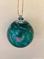 Front view of green glass ornament hanging, showing pink accents and twine loop