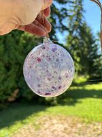 Front view of mottled purple and white glass ornament held outdoors