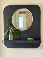 Front view of black wood wall mirror with circular mirror and shelf