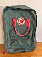 Front of green Fjällräven Kånken backpack showing logo patch, handles, front pocket and overall condition