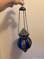 Full view of lantern hanging showing glass body, metal bands, chains and hook
