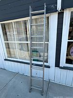 Full view of the 16ft aluminum extension ladder leaning against a windowed building exterior.