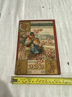 Front cover of 1892 Capital Almanac showing birds, floral designs, Capitol building, and year 1892 with measuring tape indicating size