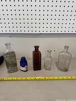 Wide shot showing all five antique bottles on shelf with measuring tape for scale.
