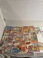 Photo showing a spread of vintage Archie comic books from series including Betty, Veronica, Jughead, Archie, and Little Archie, laid out on a flat surface.