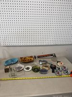 Overview of entire lot of vintage ashtrays, bar taps, Zippo box decorations and other items spread on white surface with pegboard background.