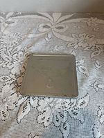 Top view of the metal case lid displaying an embossed bird design and some engraved text along the top edge, showcasing the condition of the case surface with age related wear.