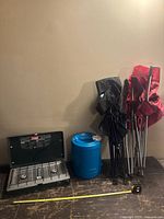 Wide view of all items: Coleman stove, blue water jug, and two folding chairs in black and red leaning against wall.