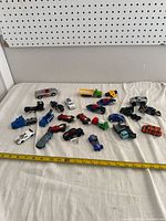 Full view of all 20 diecast toy vehicles spread on white cloth with measuring tape indicating size.