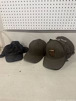 Lot display showing three plain baseball hats in black and olive green and one olive green hat with ADK patch