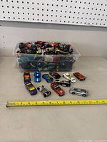 Overview of vintage and sports style toy cars displayed in front of container plus a measuring tape for scale.