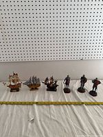 View of three model ships and four knight figurines arranged in front of pegboard with measuring tape showing approx. 7 inch length of largest ship