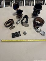 Wide shot of all items laid on a table showing belts, buckles, leather pouches, and accessories with measuring tape for size reference.